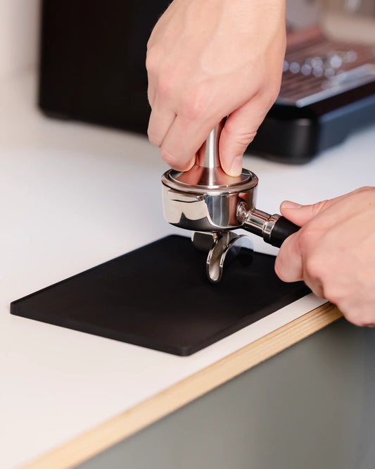 Vlakke tampermat van Barista Essentials met een portafilter en tamper