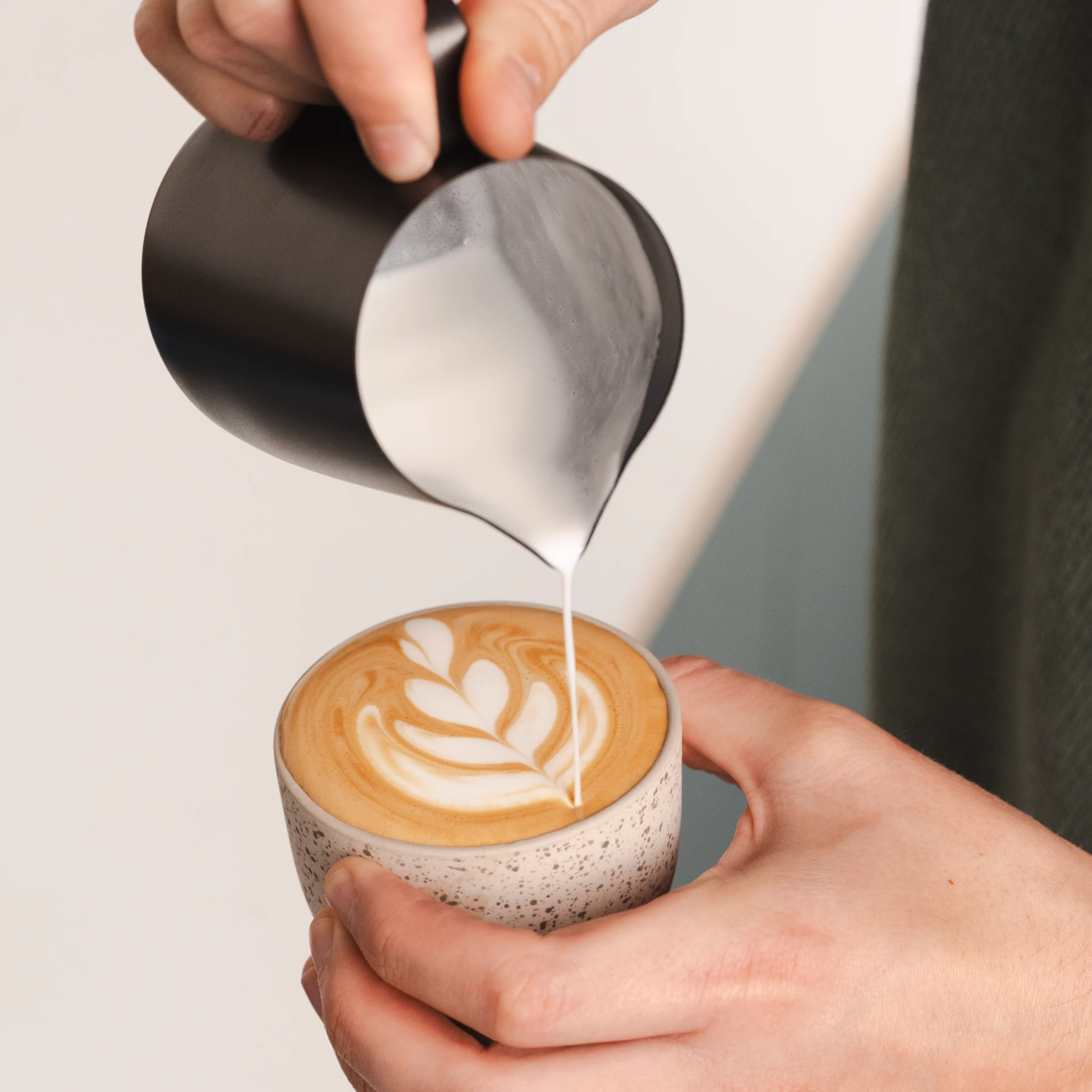 Barista schenkt latte art met melkkannetje set in het zwart voor één en twee cappuccino