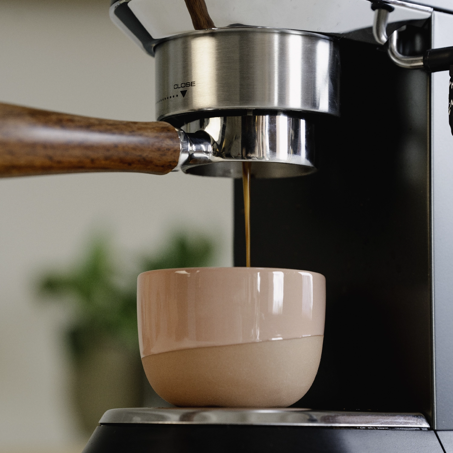 Espresso stroomt uit de Barista Essentials 51mm naked portafilter met houten handvat in een roze kopje, bevestigd aan een DeLonghi Dedica espressomachine.
