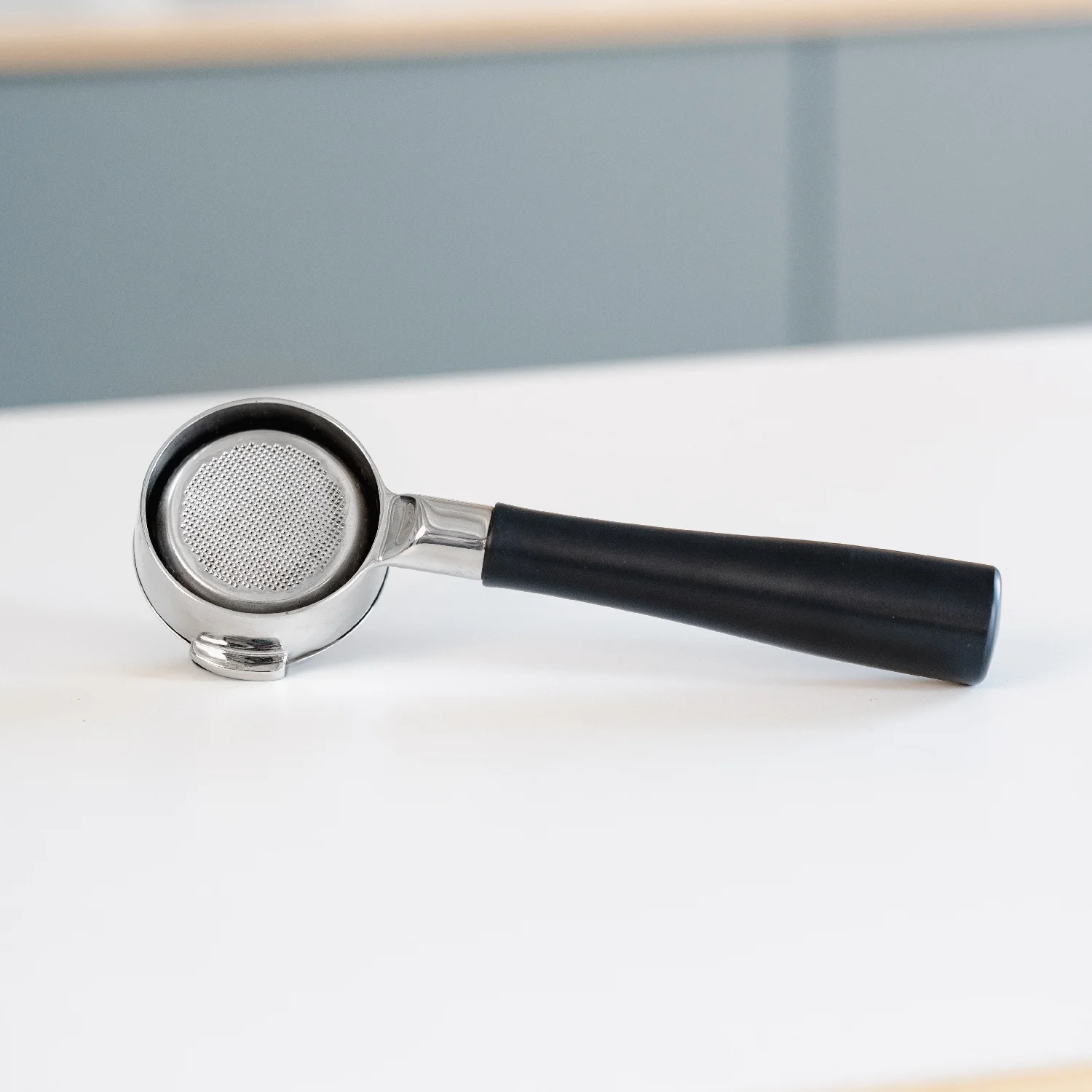 Zwarte 58mm naked portafilter van Barista Essentials liggend op een witte tafel, bedoeld voor gebruik met een Bezzera espressomachine.